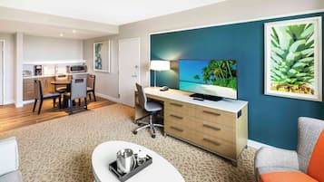 A modern hotel room with a dining area, a TV, and a large plant.