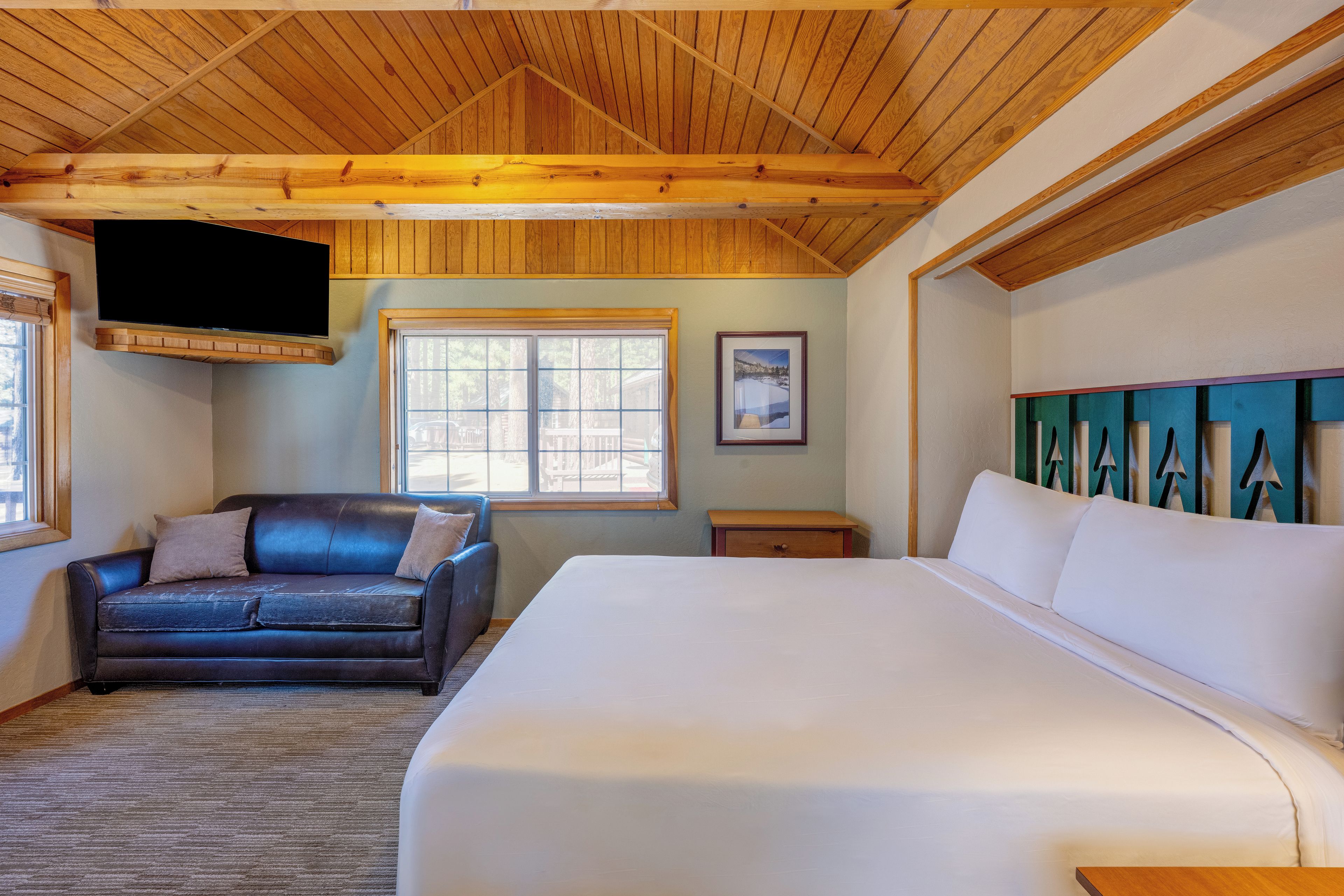 Habitación con cama, sofá, televisión en la pared y ventana con persianas.