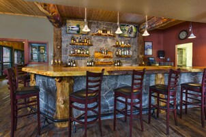 Una zona de bar con mostrador de piedra, sillas de madera y luces colgantes.
