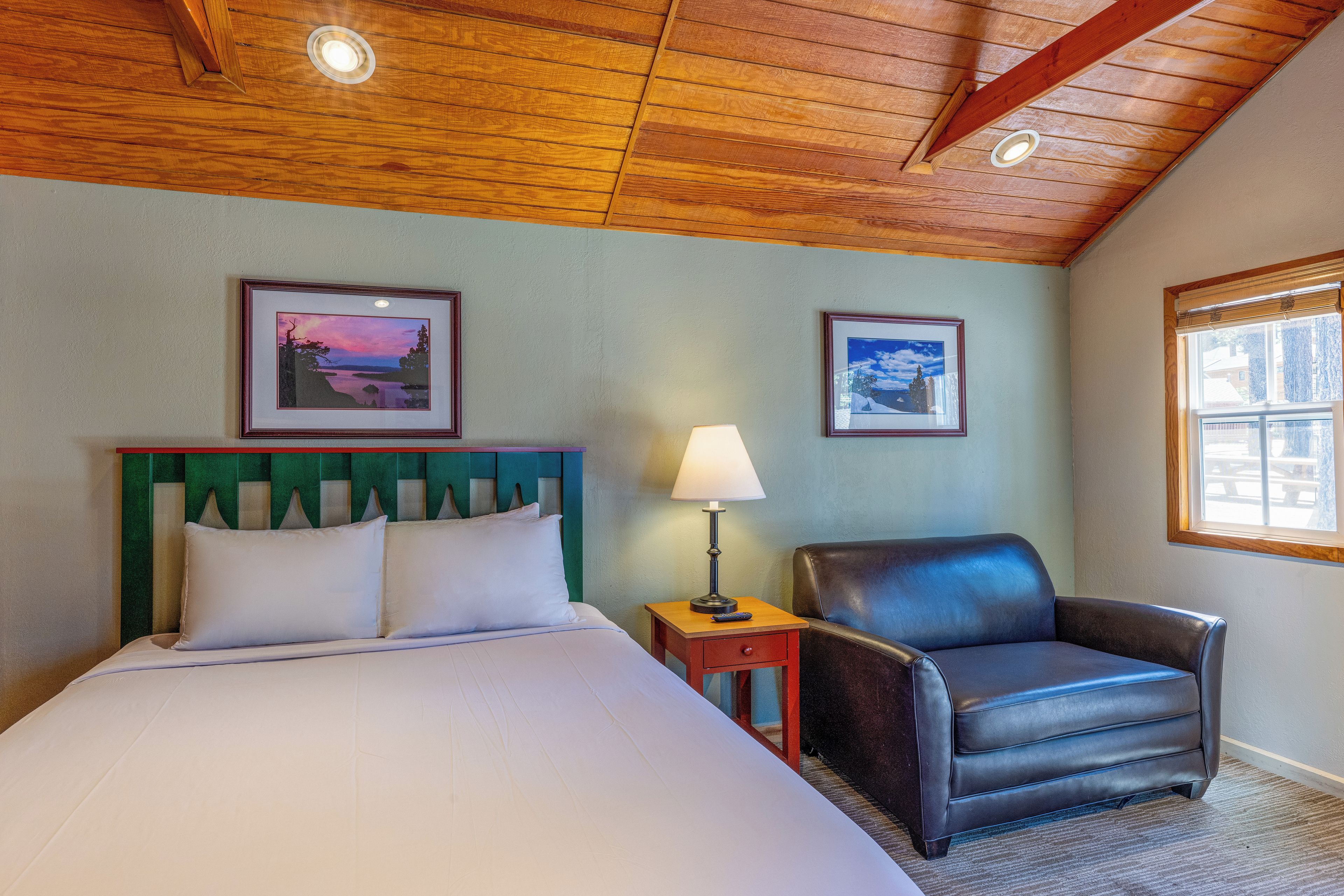 Een hotelkamer met een bed, een stoel, een nachtkastje en twee ingekaderde foto's aan de muur.
