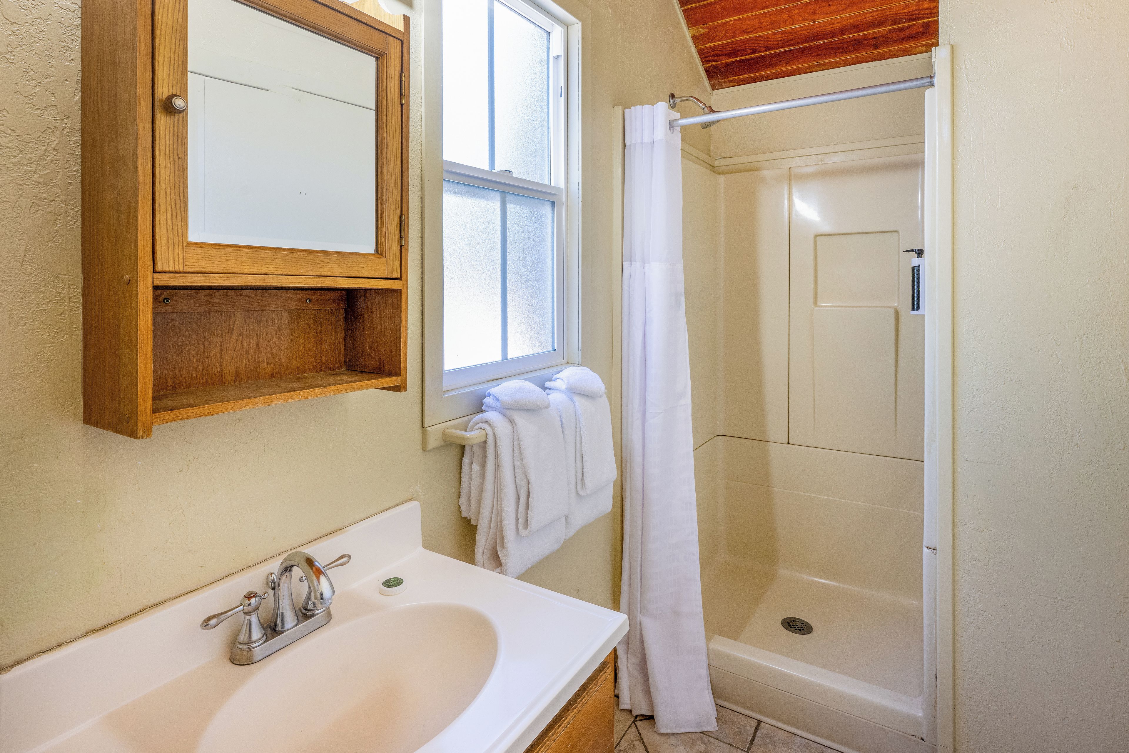 Un baño con lavamanos blanco, un espejo, ducha con puerta de vidrio y una ventana.