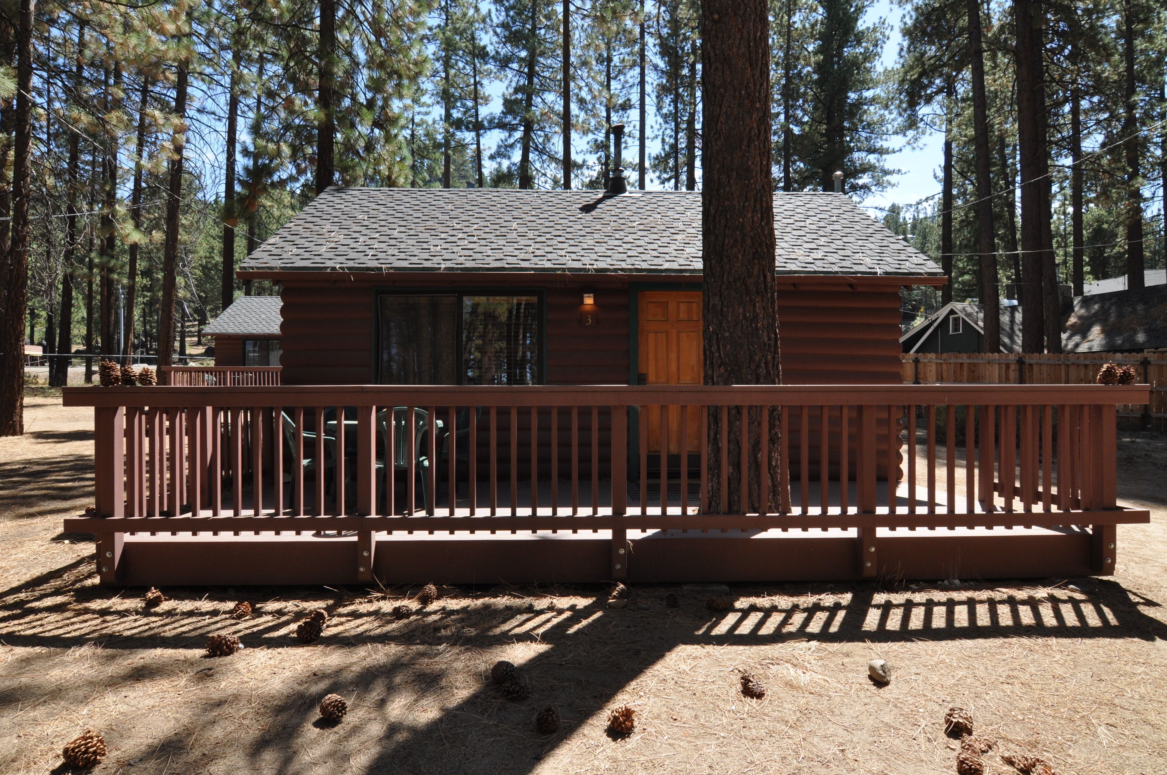 A cabin with a wooden deck, surrounded by pine trees.