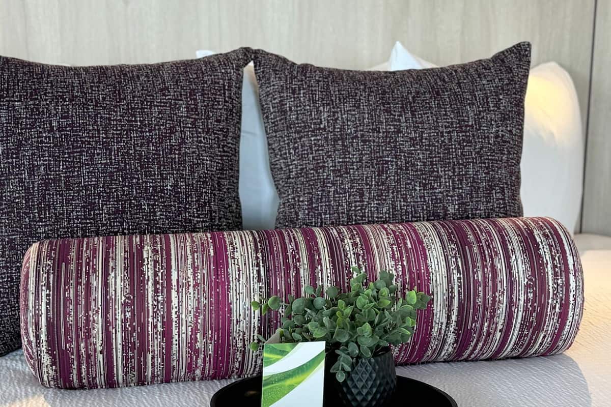 A bed with two square pillows and a cylindrical pillow.