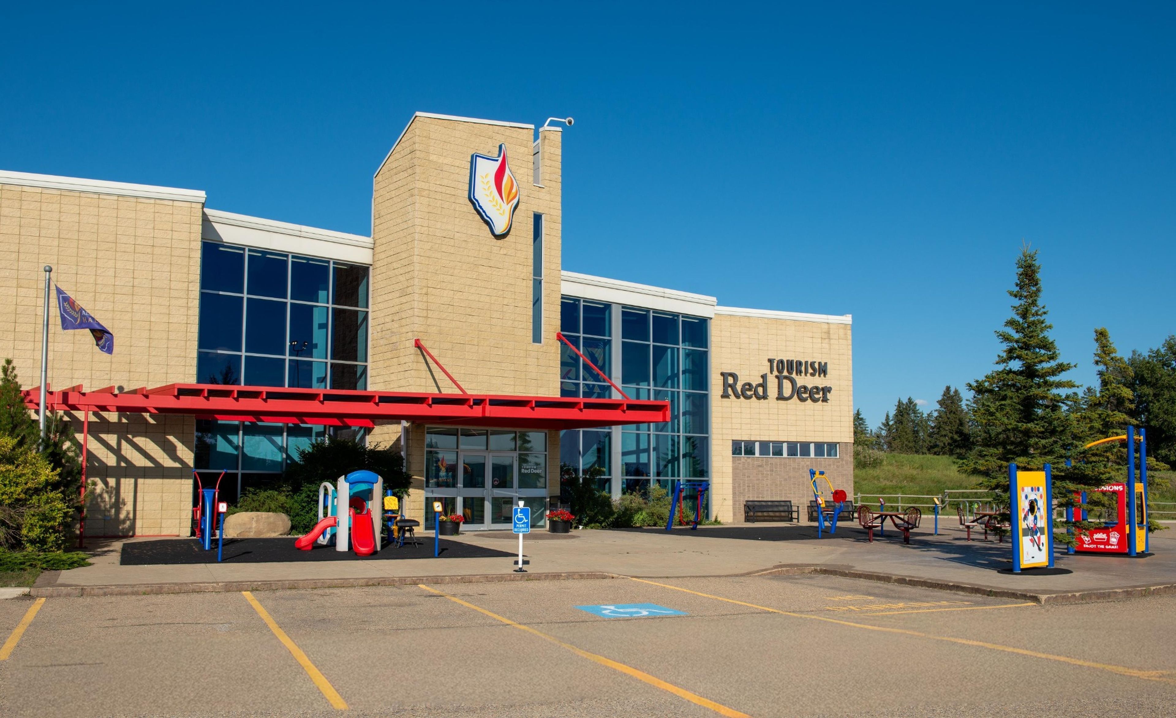 A building with a sign reading 'Tourism Red Deer' and a playground with a red slide.