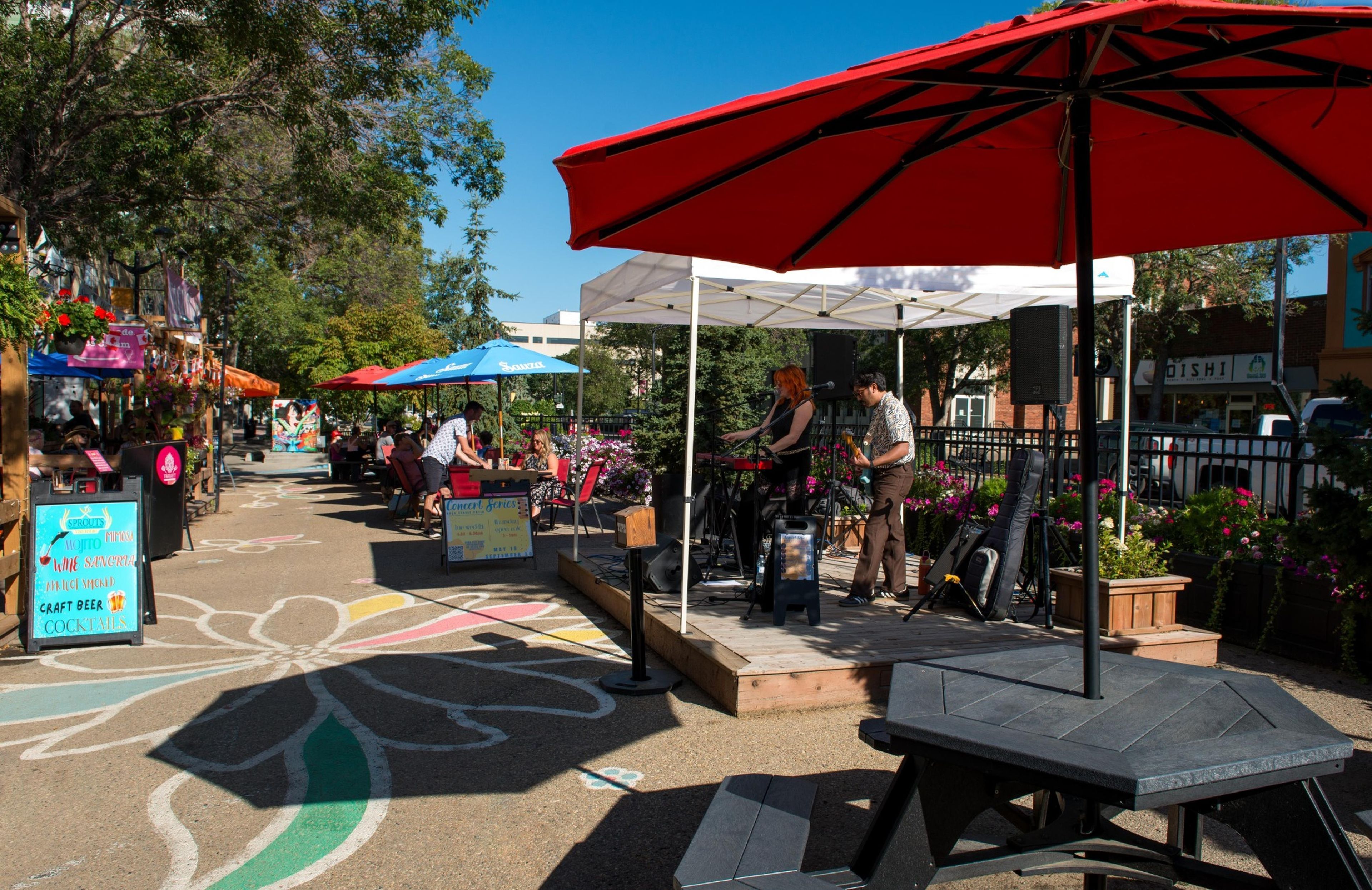 An outdoor market with stalls, a stage for live music, and a colorful pavement design.