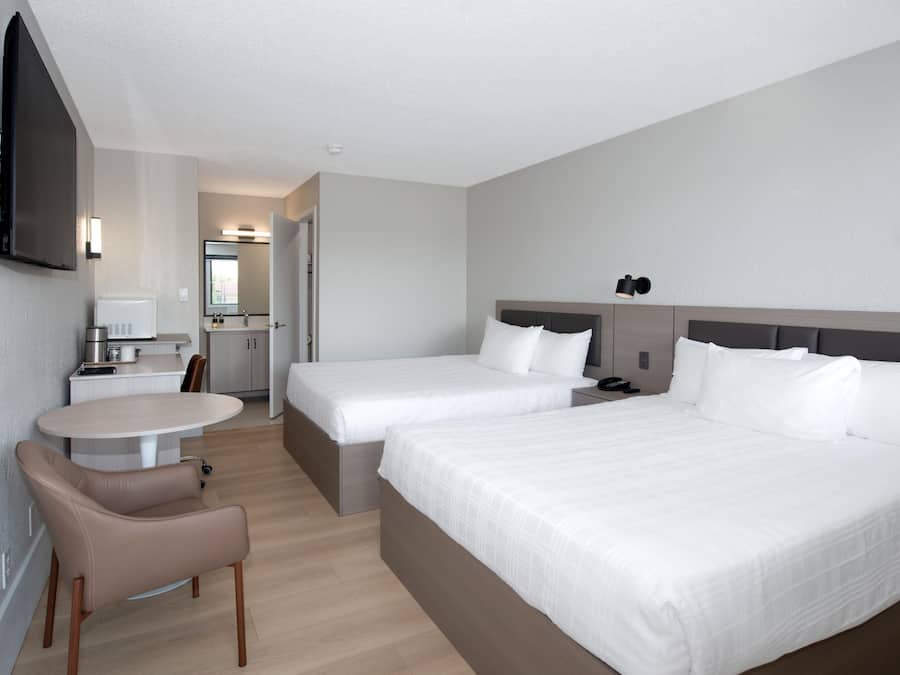 A hotel room with two beds, a desk, a chair, a TV, and a bathroom.