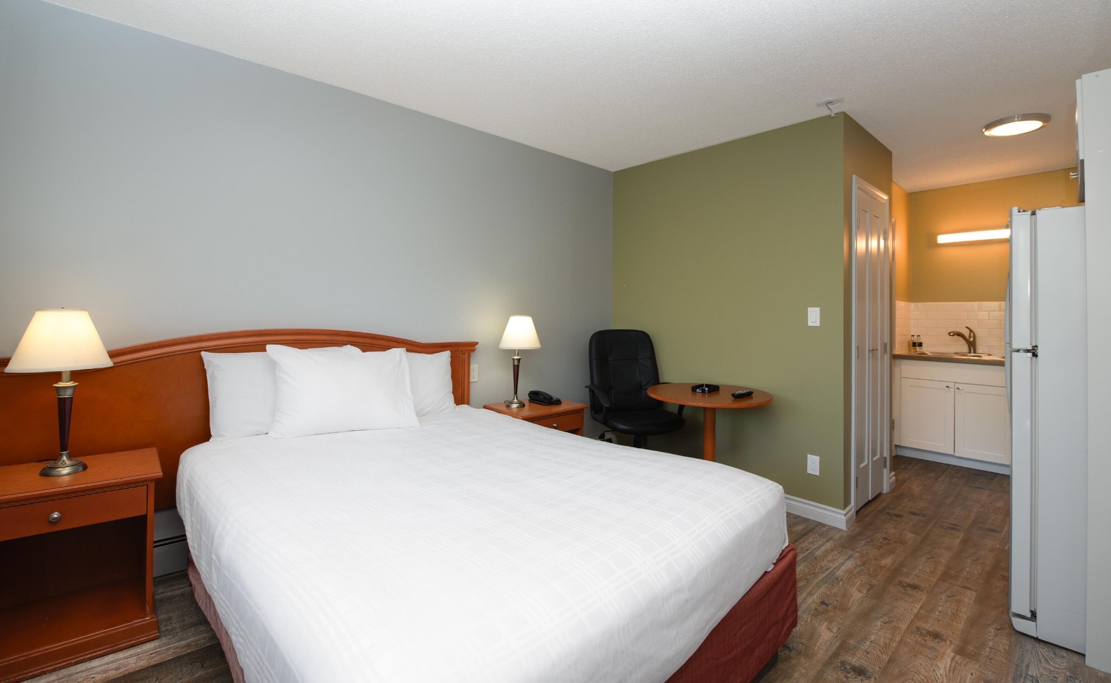 Una habitación de hotel con cama, lámparas de noche, una silla, una mesita y una kitchenette.