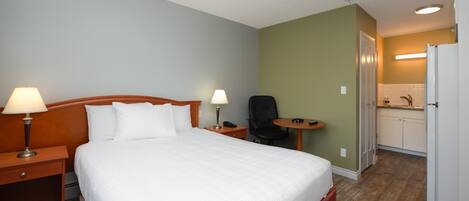 Una habitación de hotel con cama, lámparas de noche, una silla, una mesita y una kitchenette.