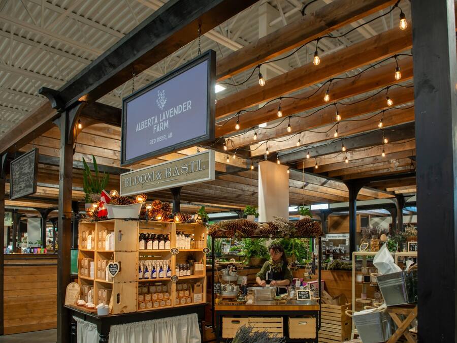 Paikallisten tuotteiden myyntipöytä, jossa on puiset hyllyt täynnä tuotteita, kyltti, jossa lukee Alberta Lavender Farm, ja maalaishenkinen sisustus, jossa on esillä olevat palkit ja koristeelliset valonauhat.