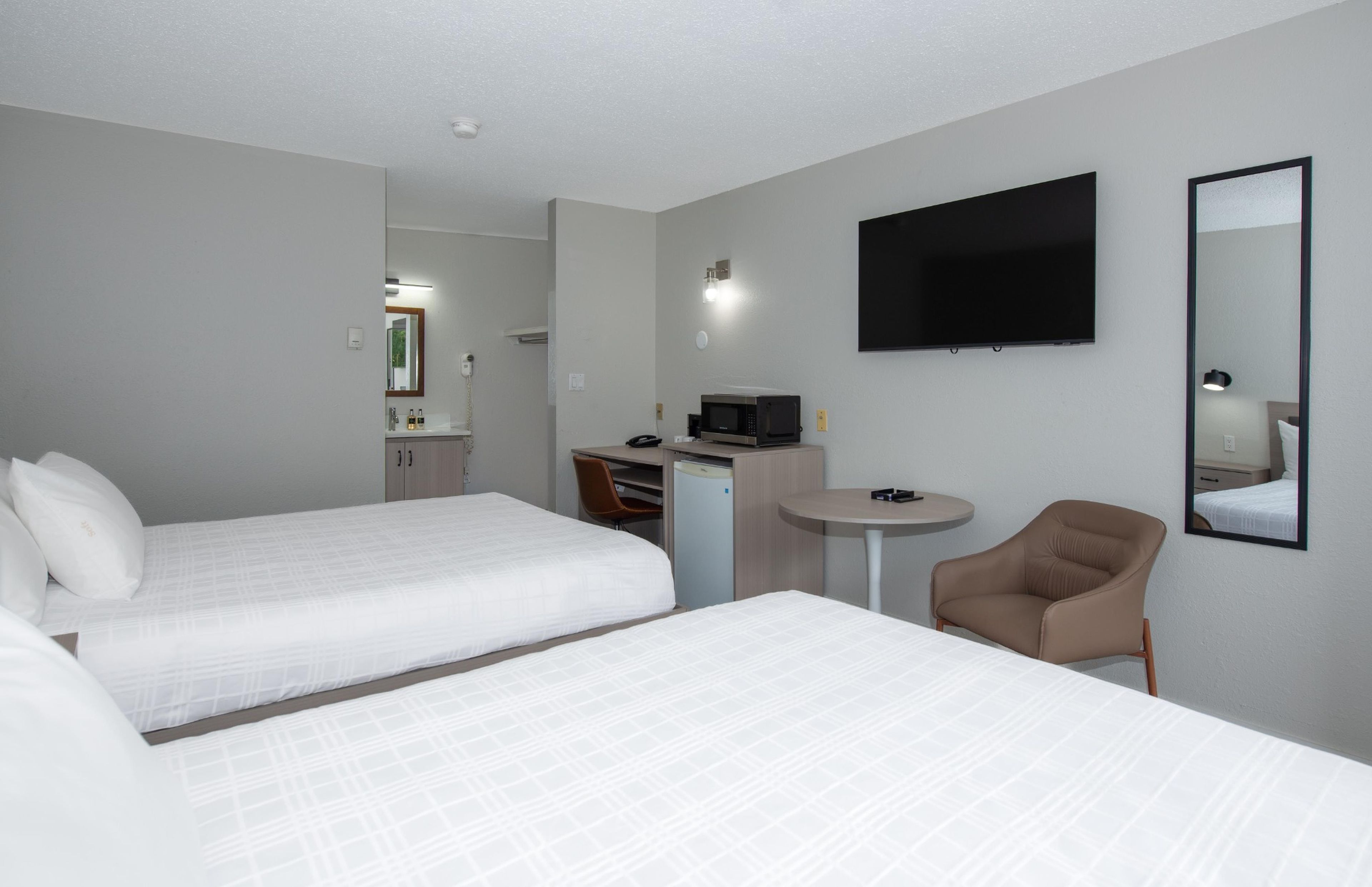 A hotel room with two beds, a desk, a chair, a flat-screen TV, and a small table.