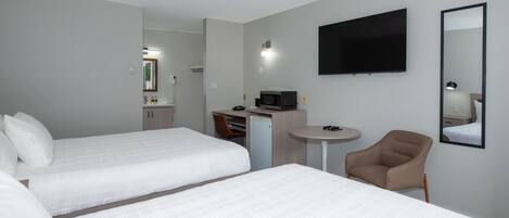 A hotel room with two beds, a desk, a chair, a flat-screen TV, and a small table.