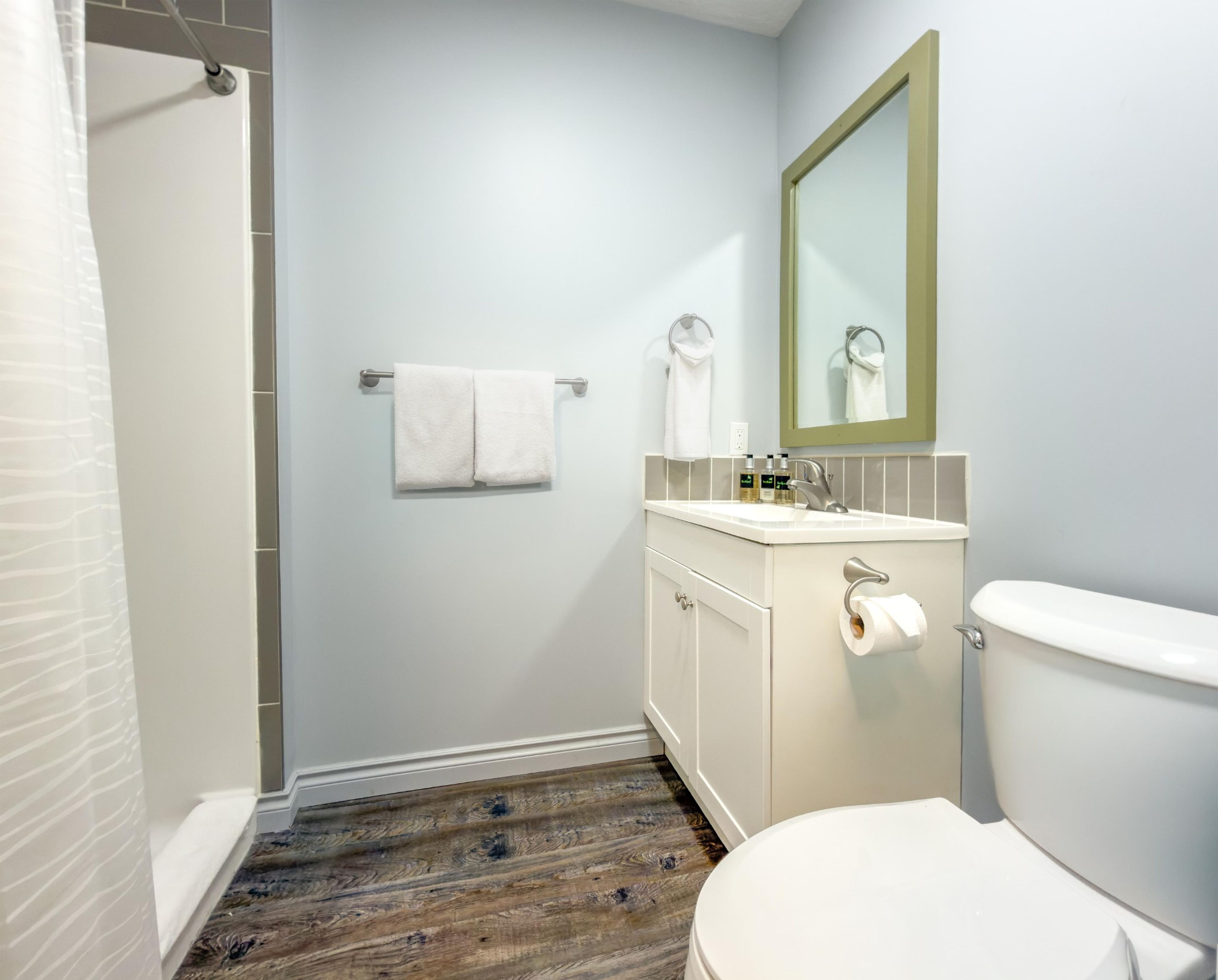 Ein Badezimmer mit Toilette, Waschbecken, Spiegel, Handtuchhalter und Duschbereich.