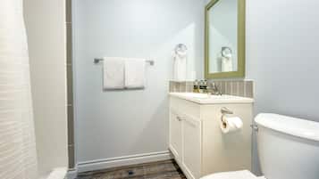 Ein Badezimmer mit Toilette, Waschbecken, Spiegel, Handtuchhalter und Duschbereich.