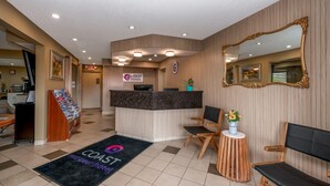 A hotel reception area with a reception desk, a waiting area with chairs, a large mirror, and a sign for 'Coast Hotels'.