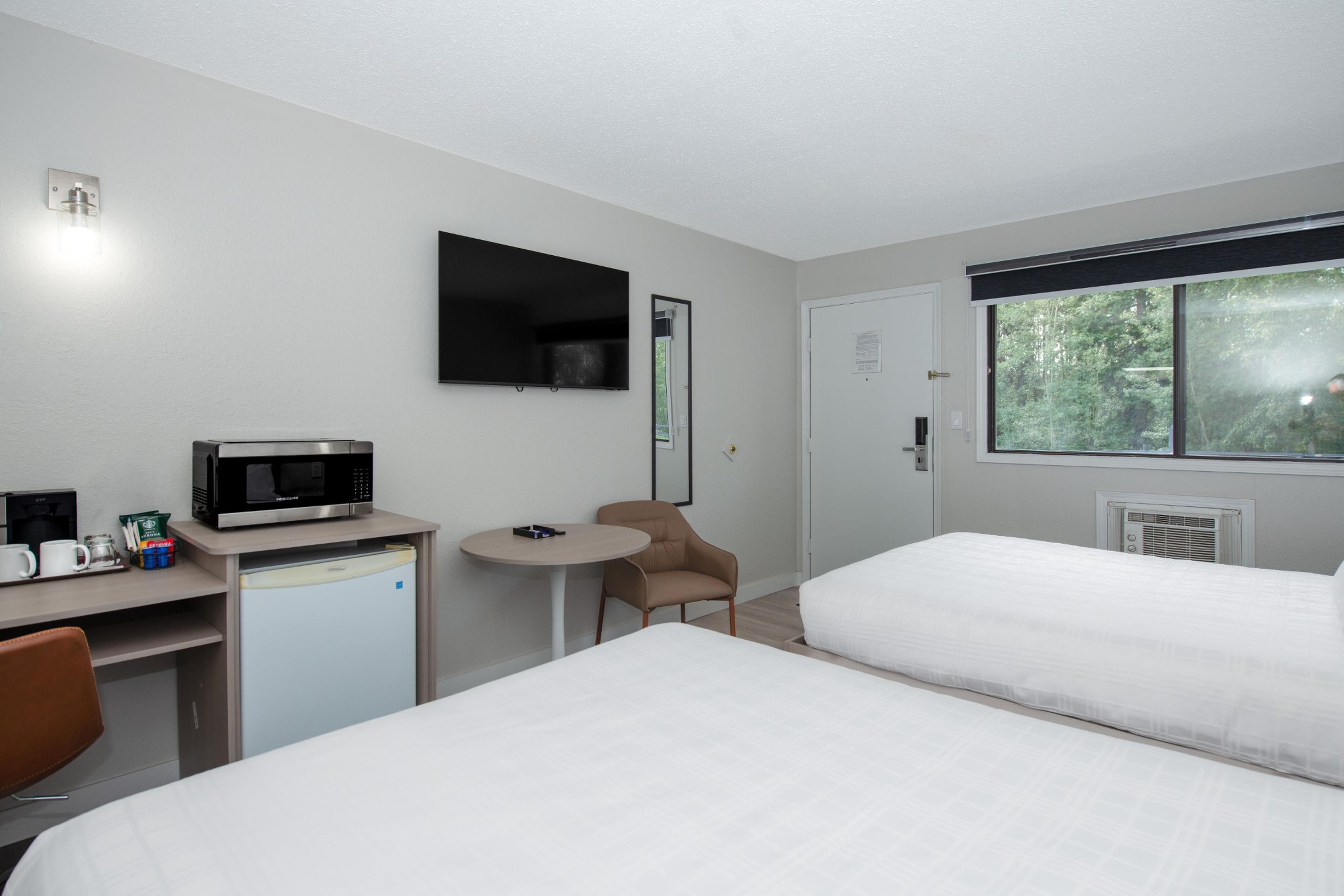 Ein Hotelzimmer mit Bett, Schreibtisch mit Mikrowelle, Stuhl und Fenster mit Blick auf Bäume.
