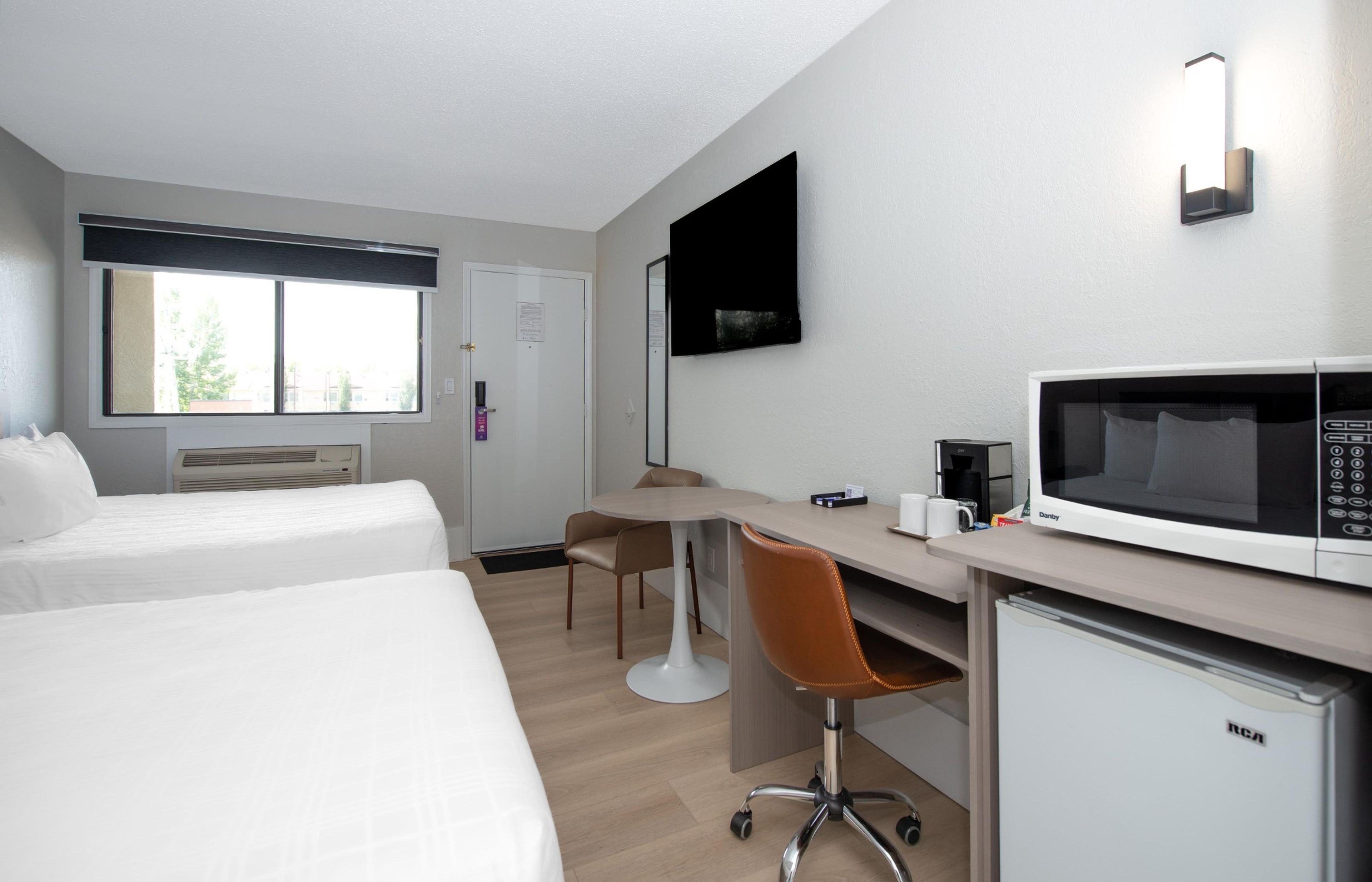 A hotel room with two beds, a desk with a chair, a microwave, and a flat-screen TV.