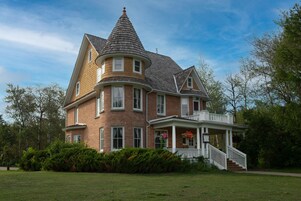 Una casa grande de dos pisos con una torre distintiva y un porche que rodea toda la edificación.