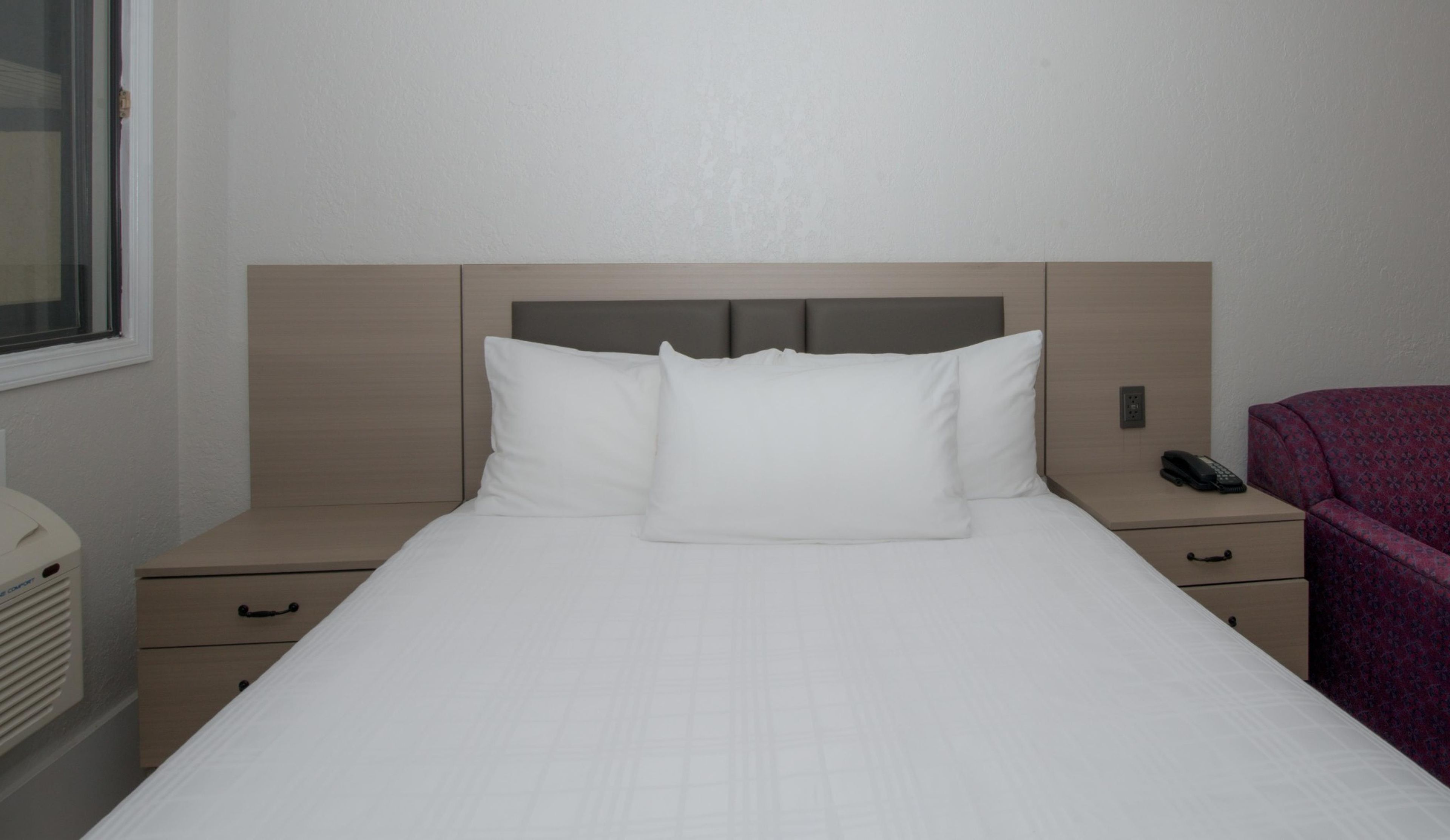 Una habitación de hotel con cama, mesita de noche, teléfono y ventana.