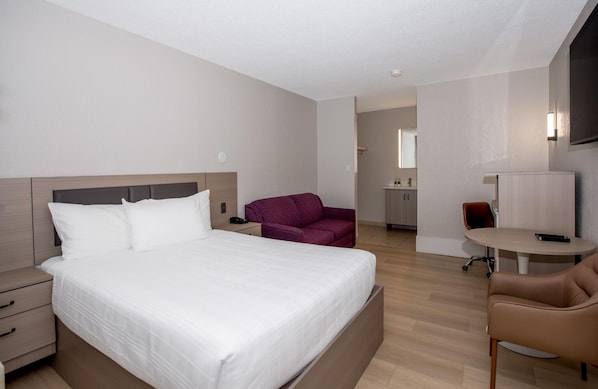 A hotel room with a large bed, a desk, a chair, a television, and a bathroom visible in the background.