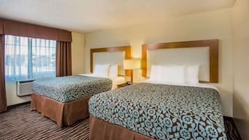 Habitación de hotel con dos camas, un ventanal con cortinas, aire acondicionado en la pared y suelo alfombrado.