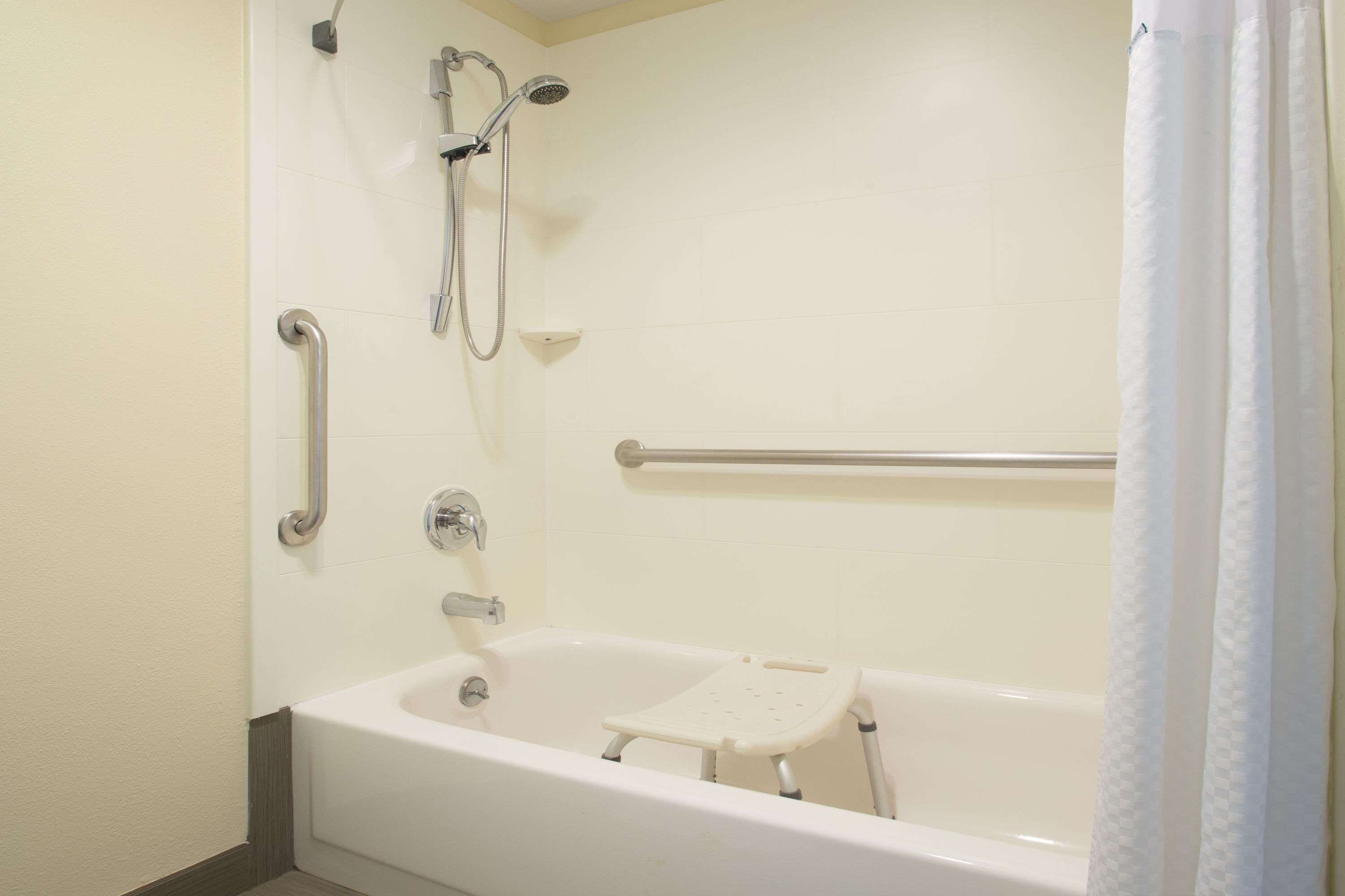 Une salle de bain équipée d’une baignoire, de barres d’appui, d’un pommeau de douche et d’un rideau de douche blanc.