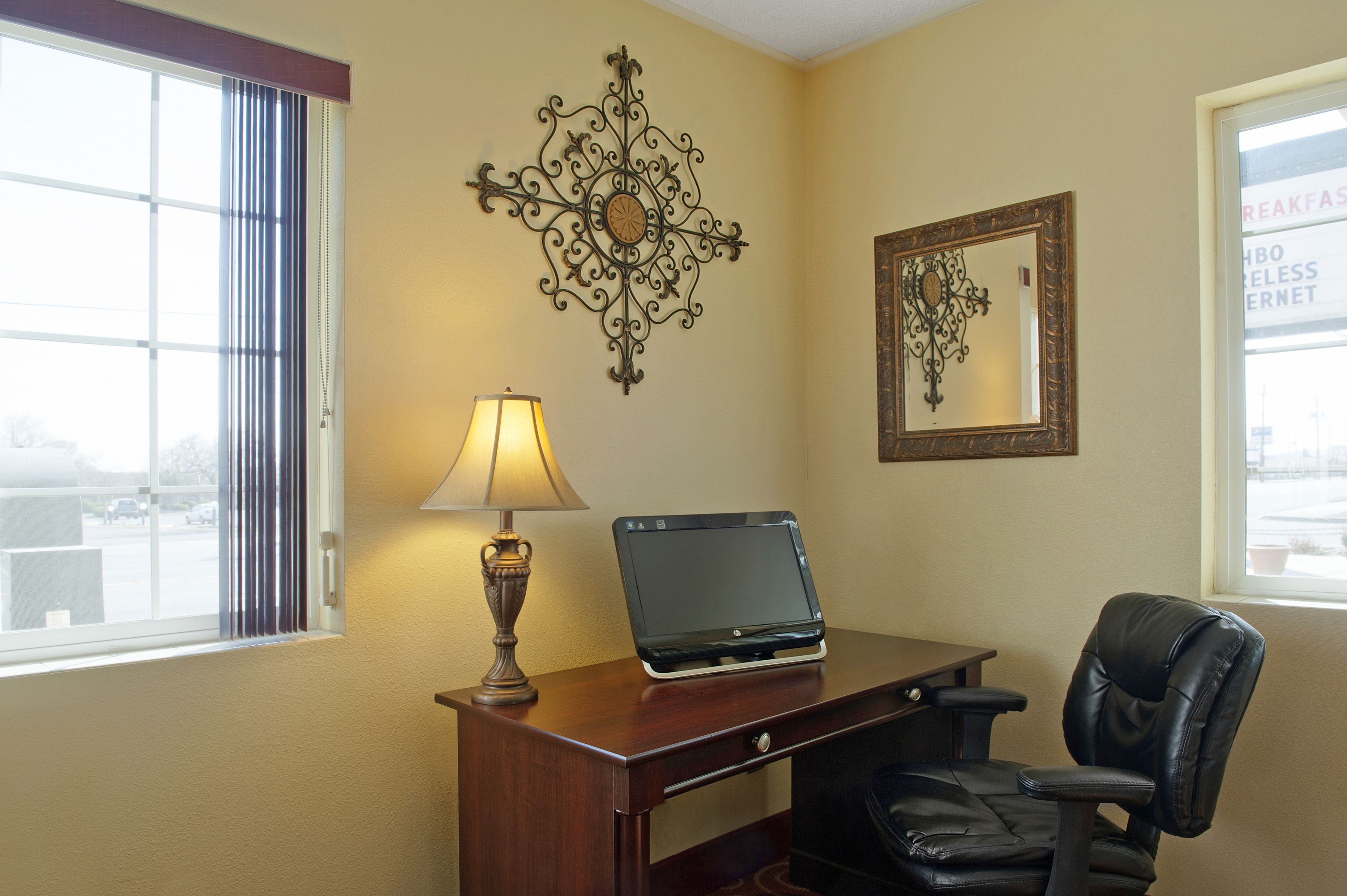 A hotel room with a desk, a laptop, a chair, a lamp, and decorative wall art.