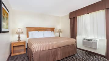Habitación de hotel con una cama, dos mesitas de noche, una ventana con cortinas y un equipo de aire acondicionado.