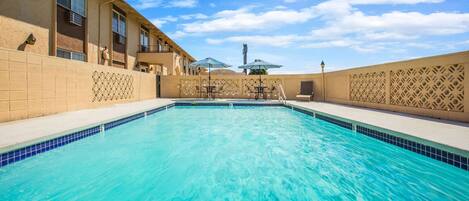 Una piscina con agua azul cristalina, rodeada de muros color beige y un suelo de baldosas.