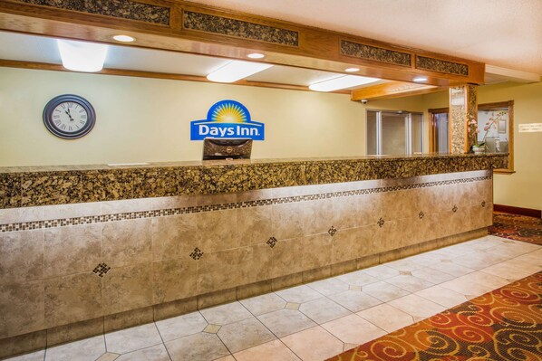 Uma área de recepção com um relógio, o letreiro Days Inn e um balcão de mármore.