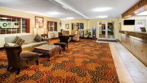 Un hall d’entrée avec un tapis à motifs, des canapés, des fauteuils, une table basse, un comptoir de réception et un téléviseur.