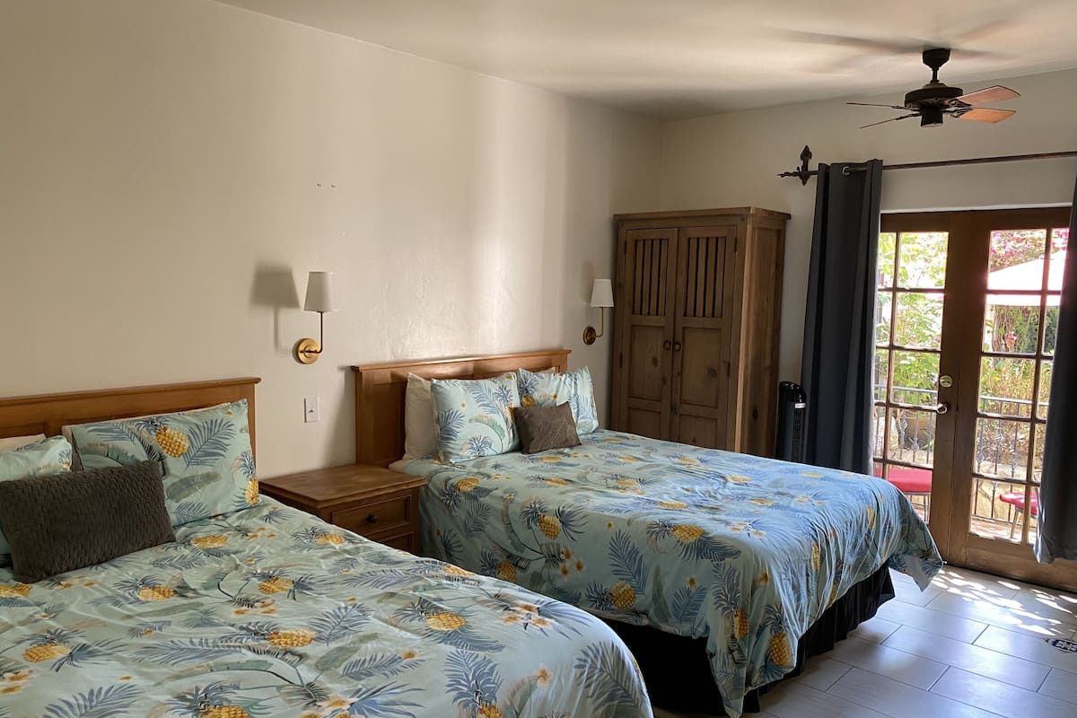 A room with two beds, a wardrobe, a ceiling fan, and a door leading to an outdoor area.