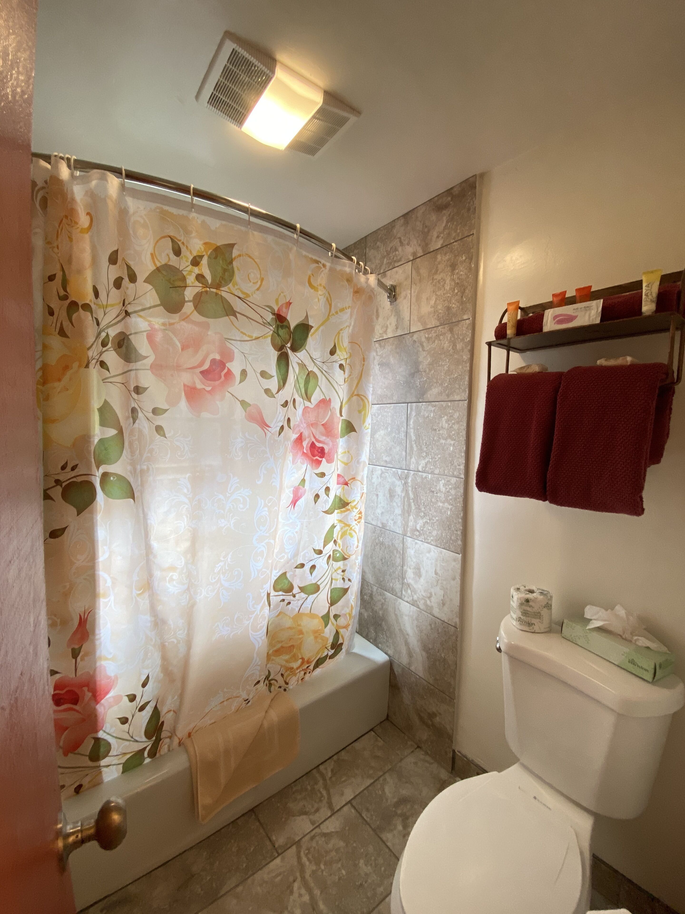 Een badkamer met douchegordijn, bad, toilet en een plank met toiletartikelen.