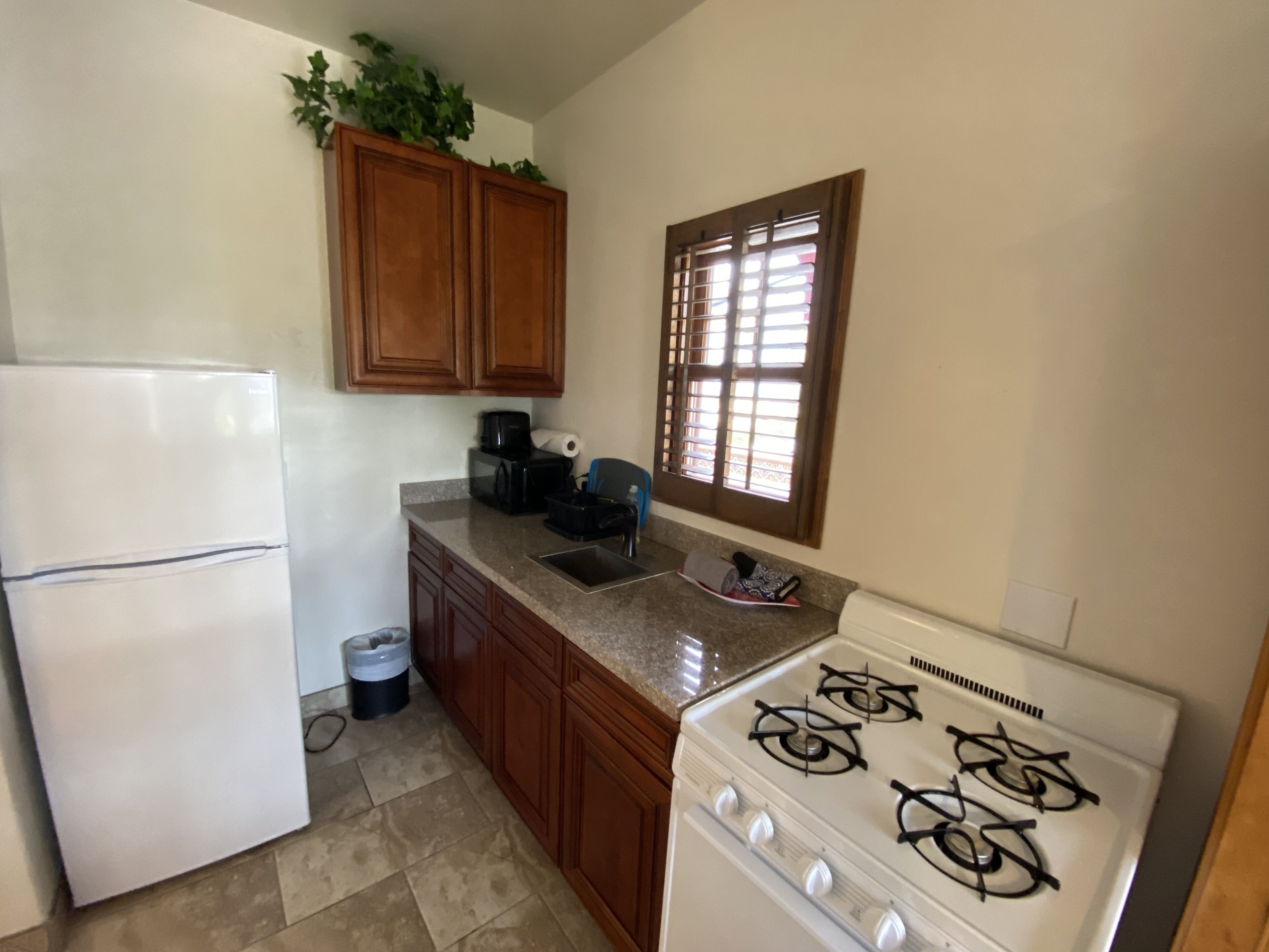 Una cocina con refrigerador, estufa, alacenas y una ventana con persianas.