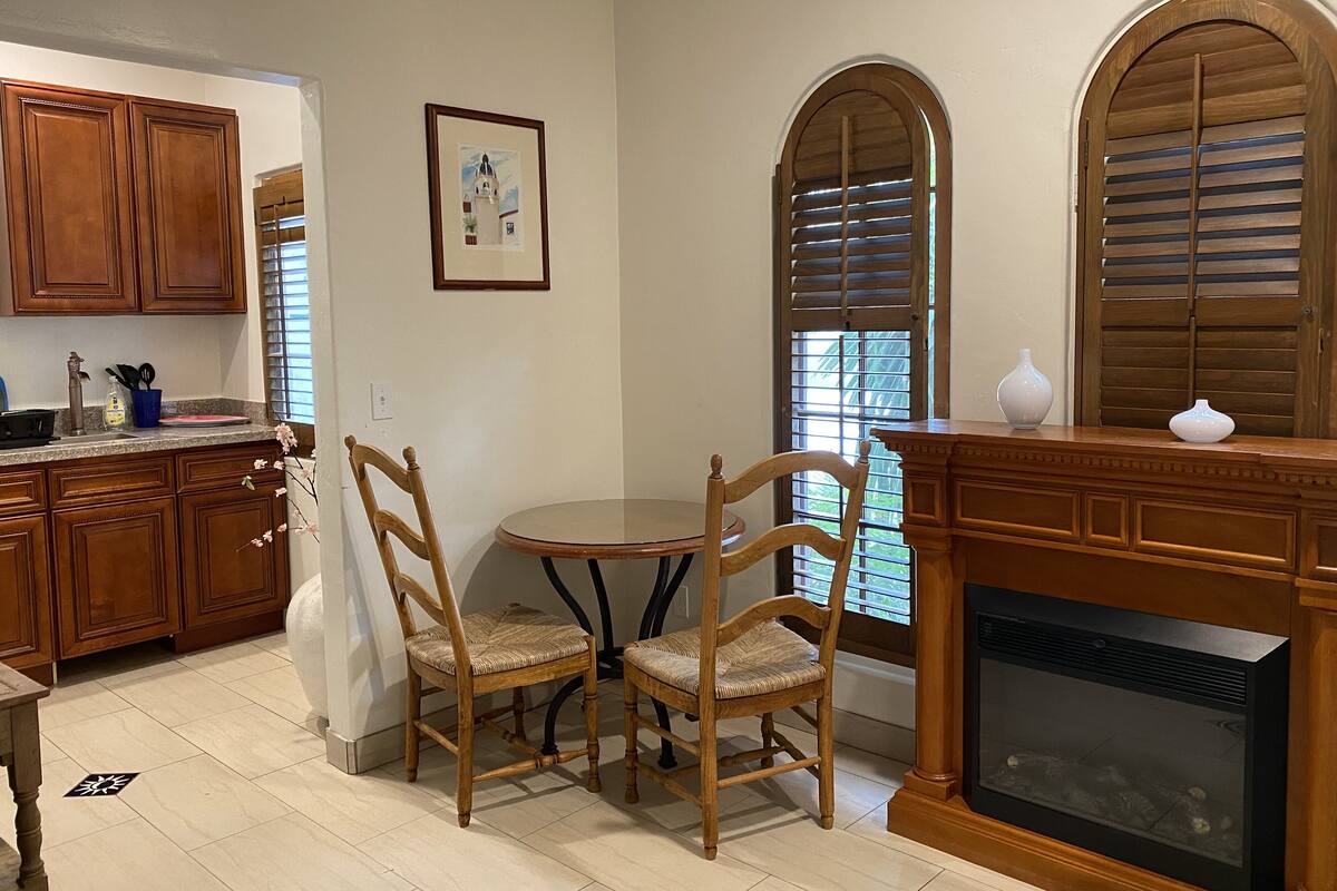 A kitchen with wooden cabinets, a dining table with chairs, a framed picture on the wall, and a fireplace.