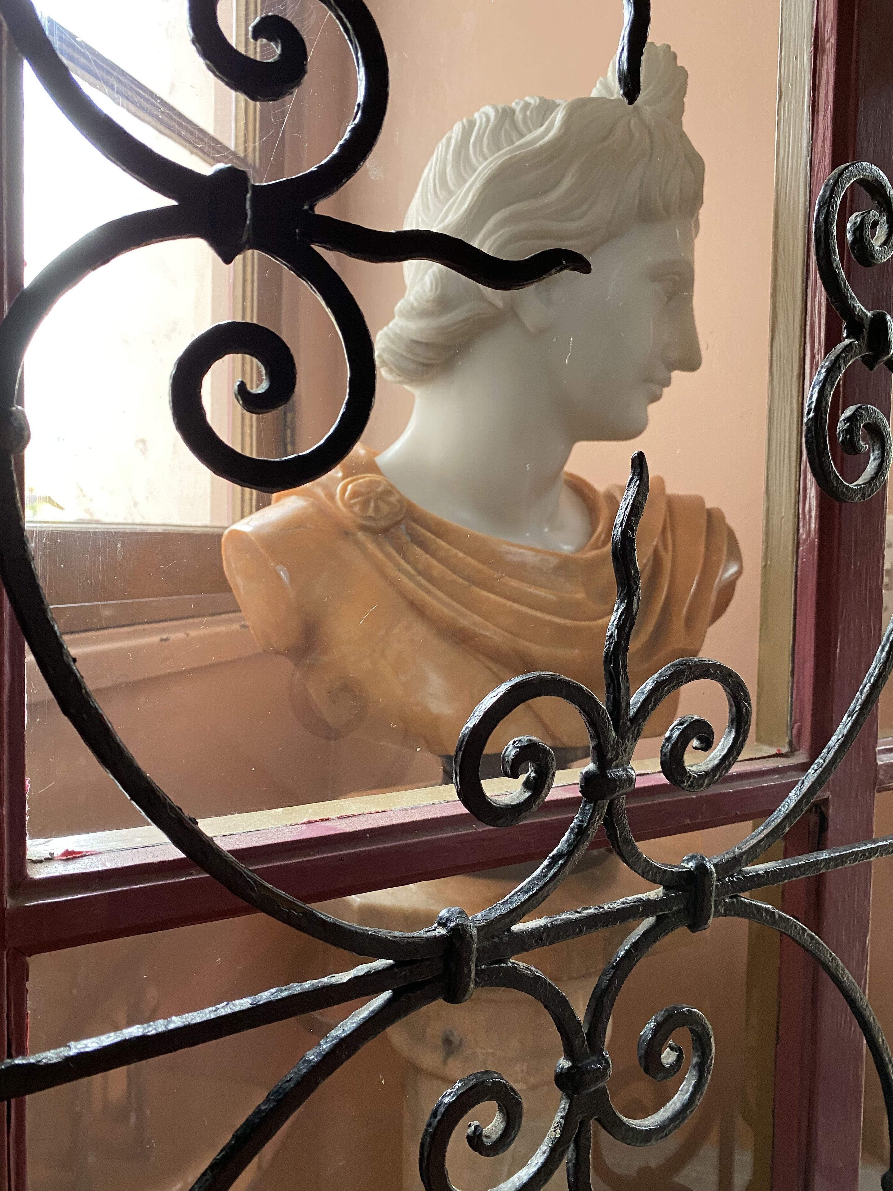 Una ventana con una reja de hierro decorativa y una escultura de busto blanco al fondo.