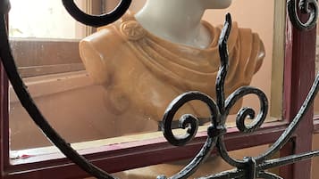 Una ventana con una reja de hierro decorativa y una escultura de busto blanco al fondo.