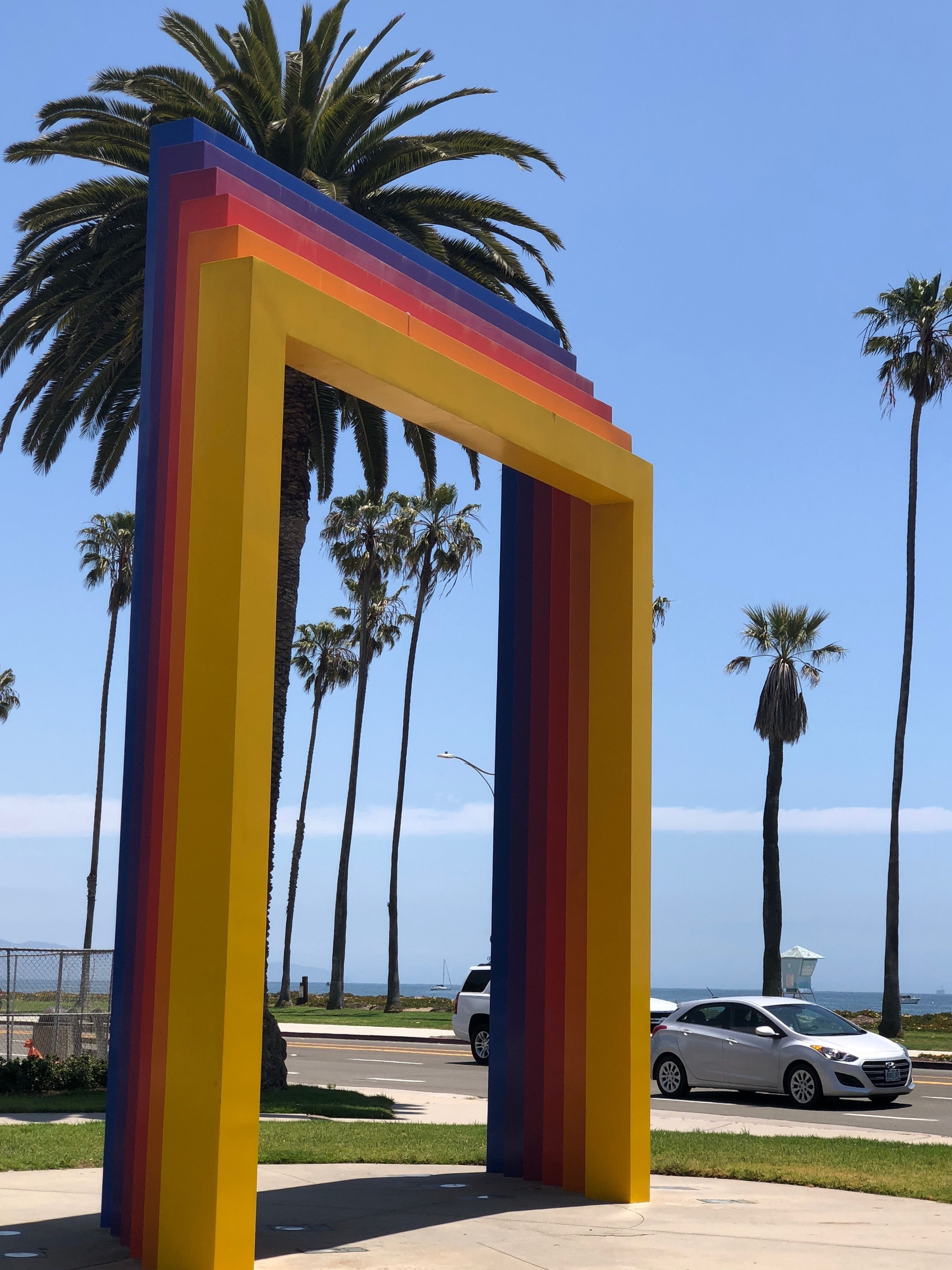 A colorful, rainbow-colored structure in a sunny outdoor setting with palm trees and a clear sky.