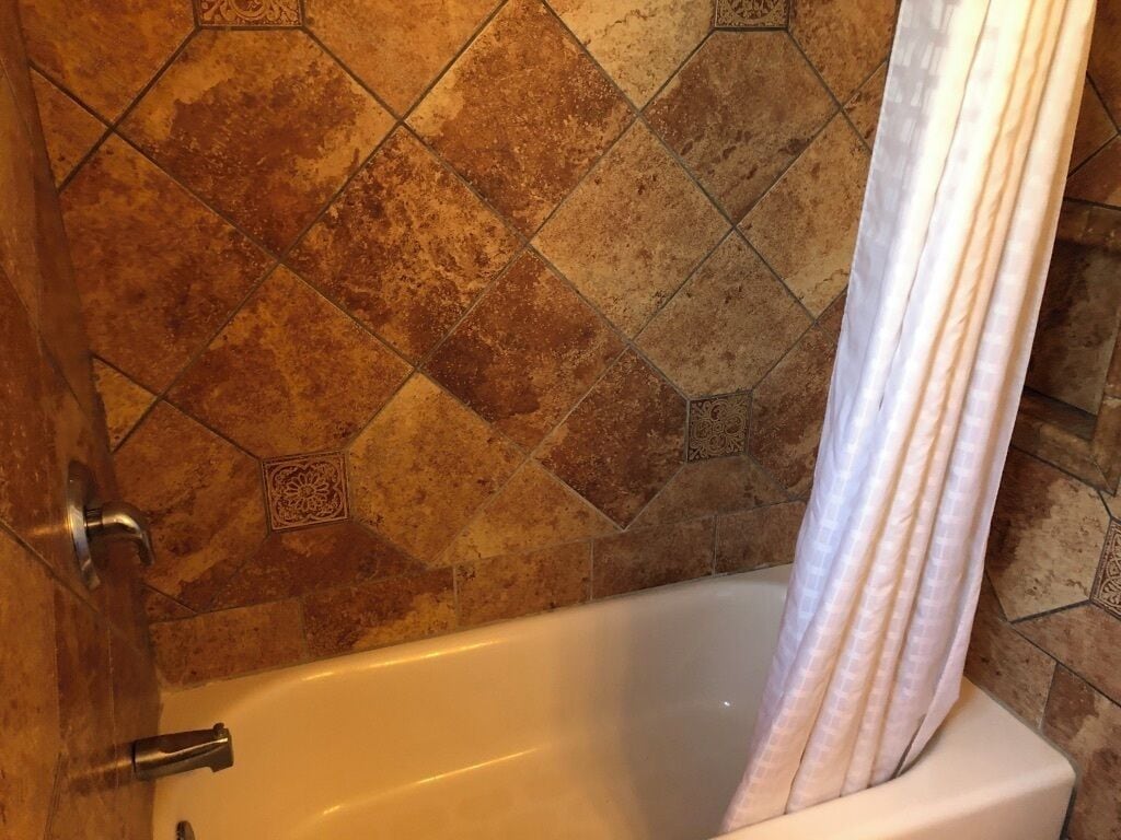 Un baño con una bañera blanca, una cortina de ducha y una pared de azulejos con un diseño geométrico.