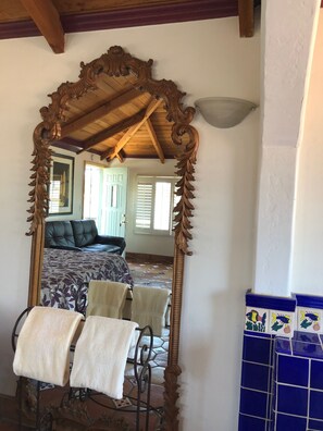 A room with a large mirror, a bed with a patterned bedspread, a chair with a towel, and a tiled wall. - Ala Mar by the Sea (Santa Barbara)