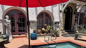 A pool area with a red umbrella, stone statues, and a spa sign. - Ala Mar by the Sea (Santa Barbara)