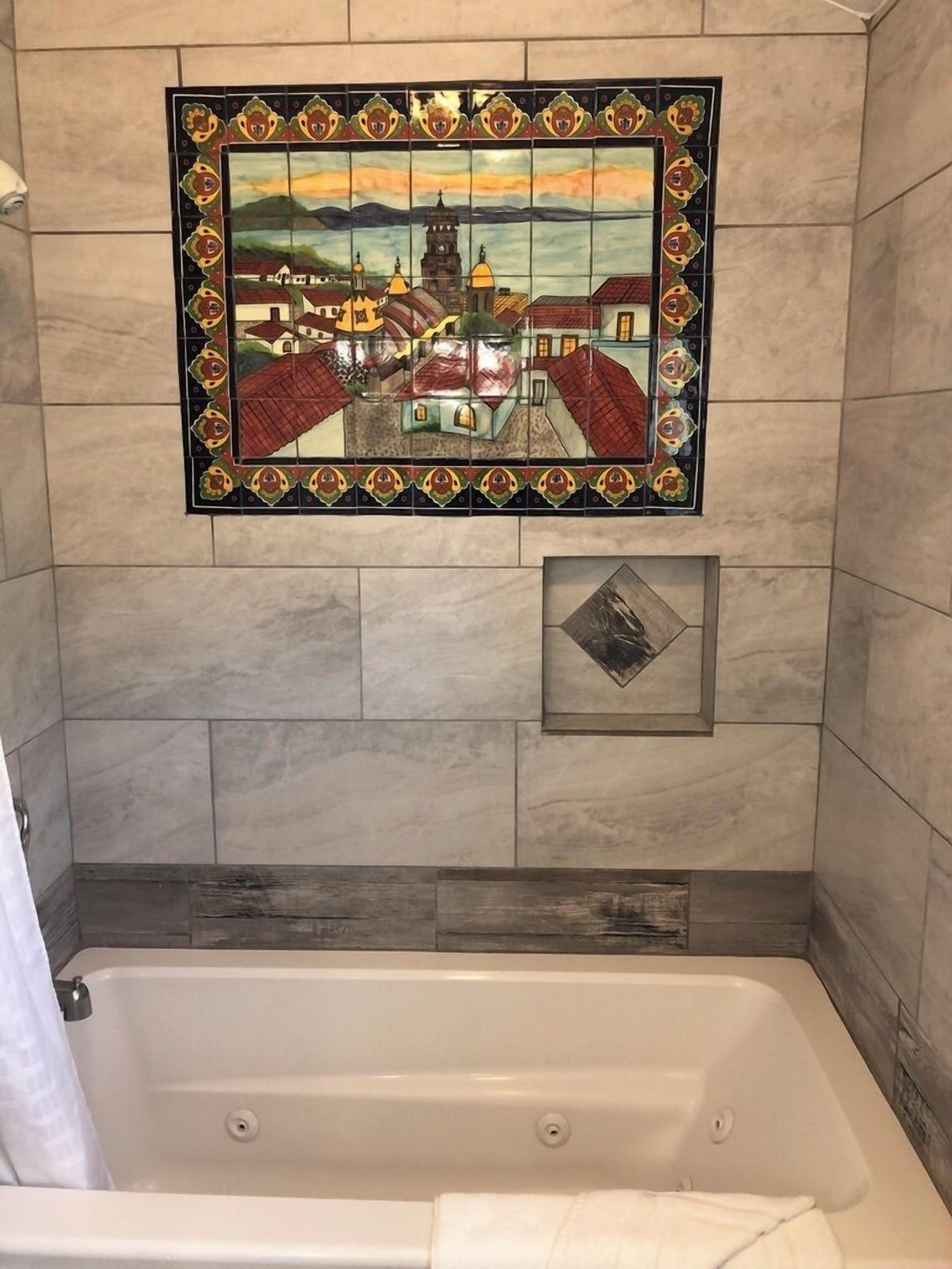 A bathroom with a mosaic tile wall, a bathtub, and a small decorative tile below the mosaic.