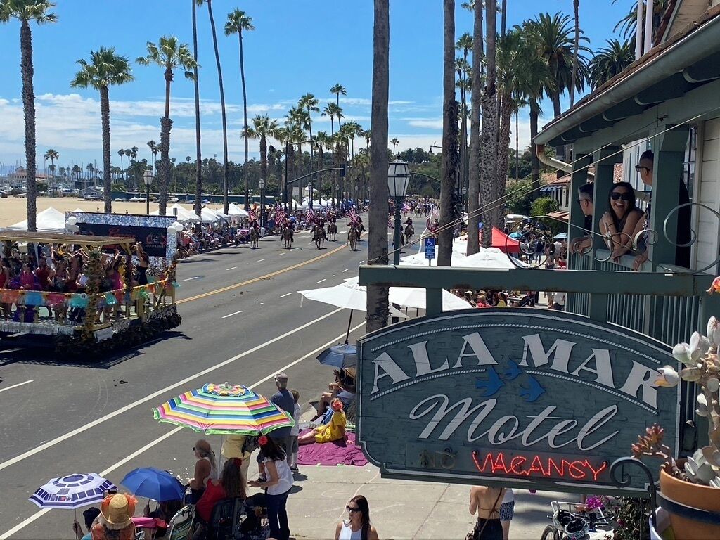 A street view with a motel sign, palm trees, and a parade.