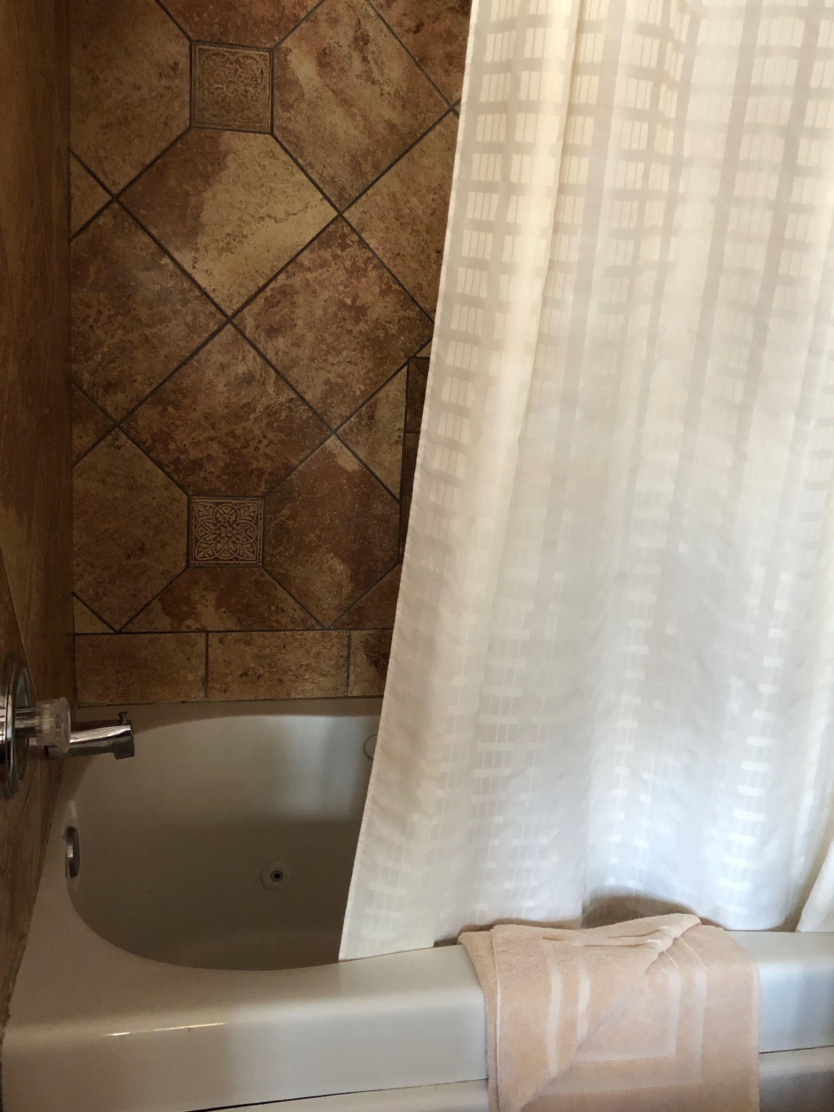 Una bañera con cortina de ducha, una toalla y un muro de azulejos con diseño geométrico.