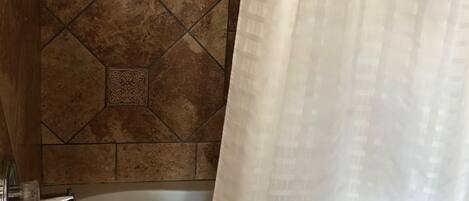Una bañera con cortina de ducha, una toalla y un muro de azulejos con diseño geométrico.