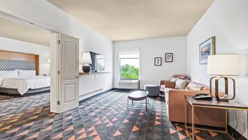 A hotel room with a bed, a sofa, a desk, a lamp, a window, and a patterned floor.