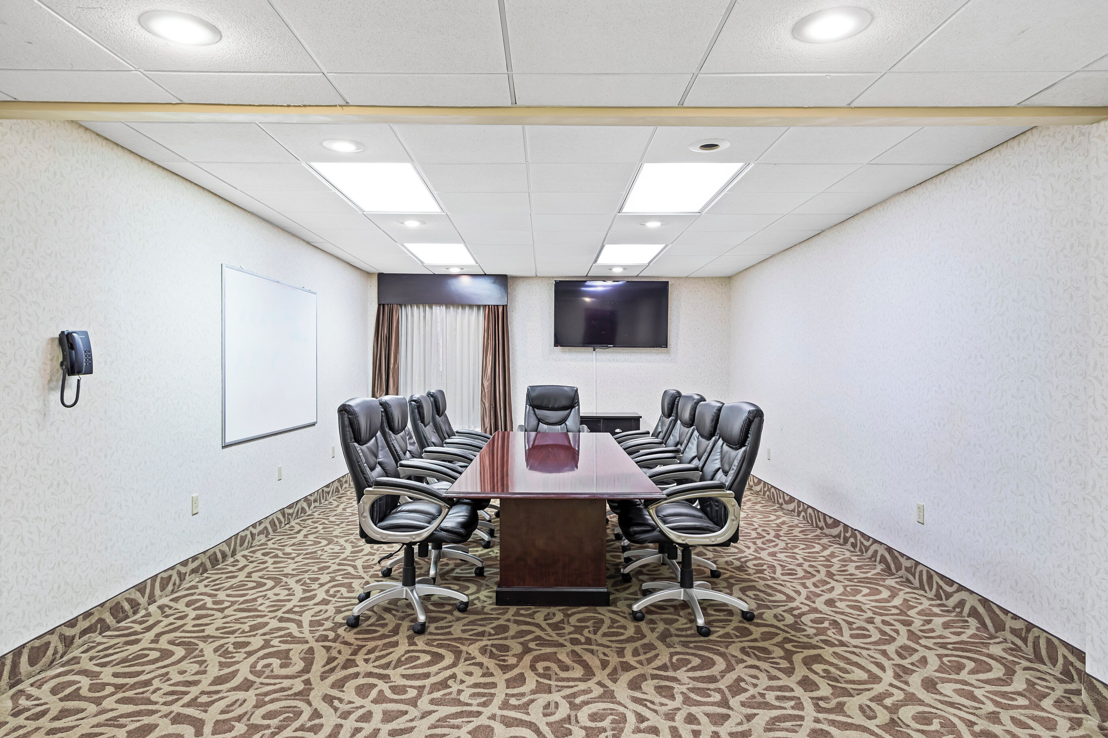 A conference room with a long table, multiple chairs, a whiteboard, a phone, and a TV on the wall.