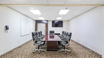 A conference room with a long table, multiple chairs, a whiteboard, a phone, and a TV on the wall.