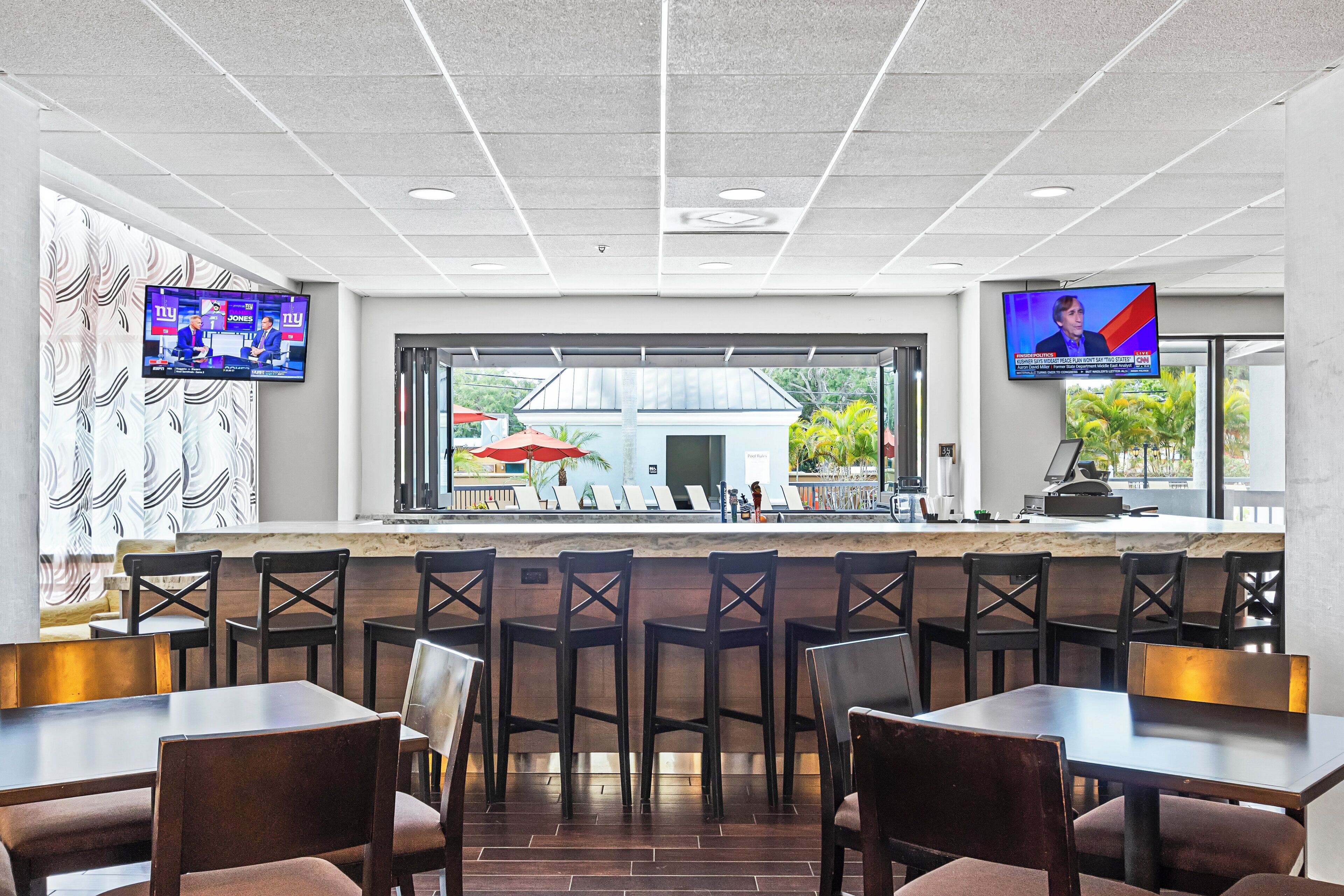 A restaurant with a bar area, multiple seating options, and two televisions mounted on the walls.