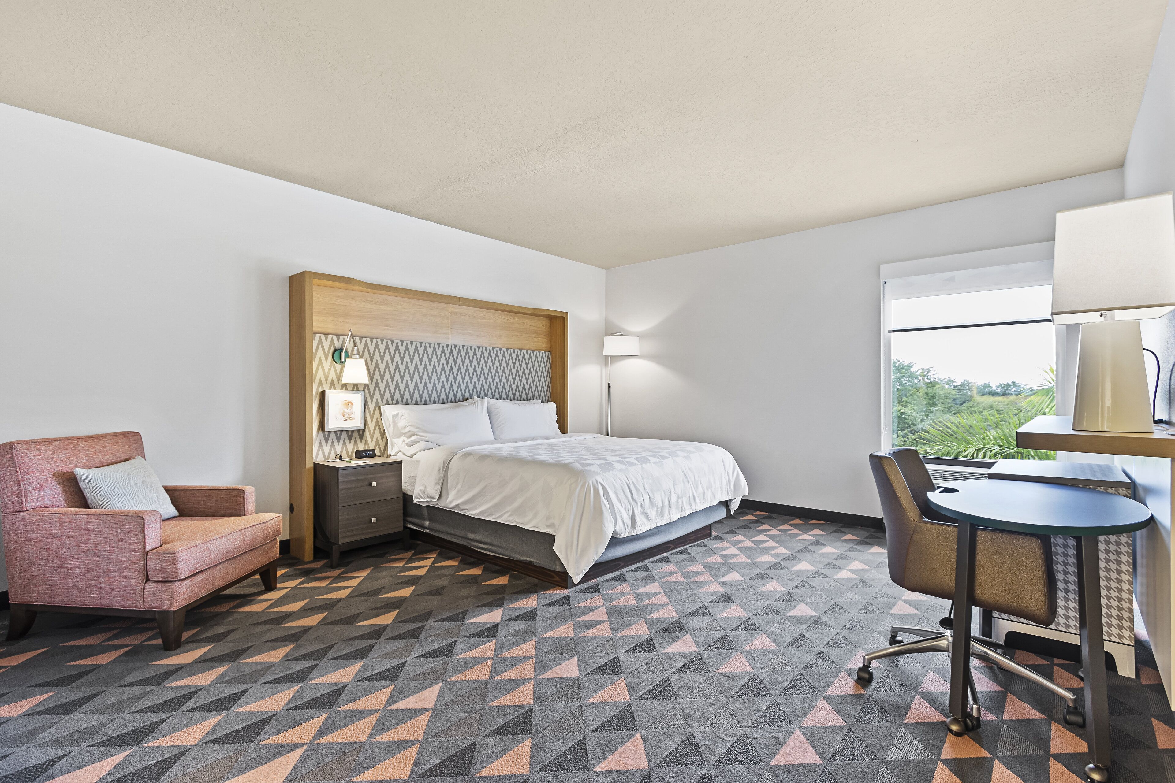 A hotel room with a bed, a desk, a chair, and a sofa.
