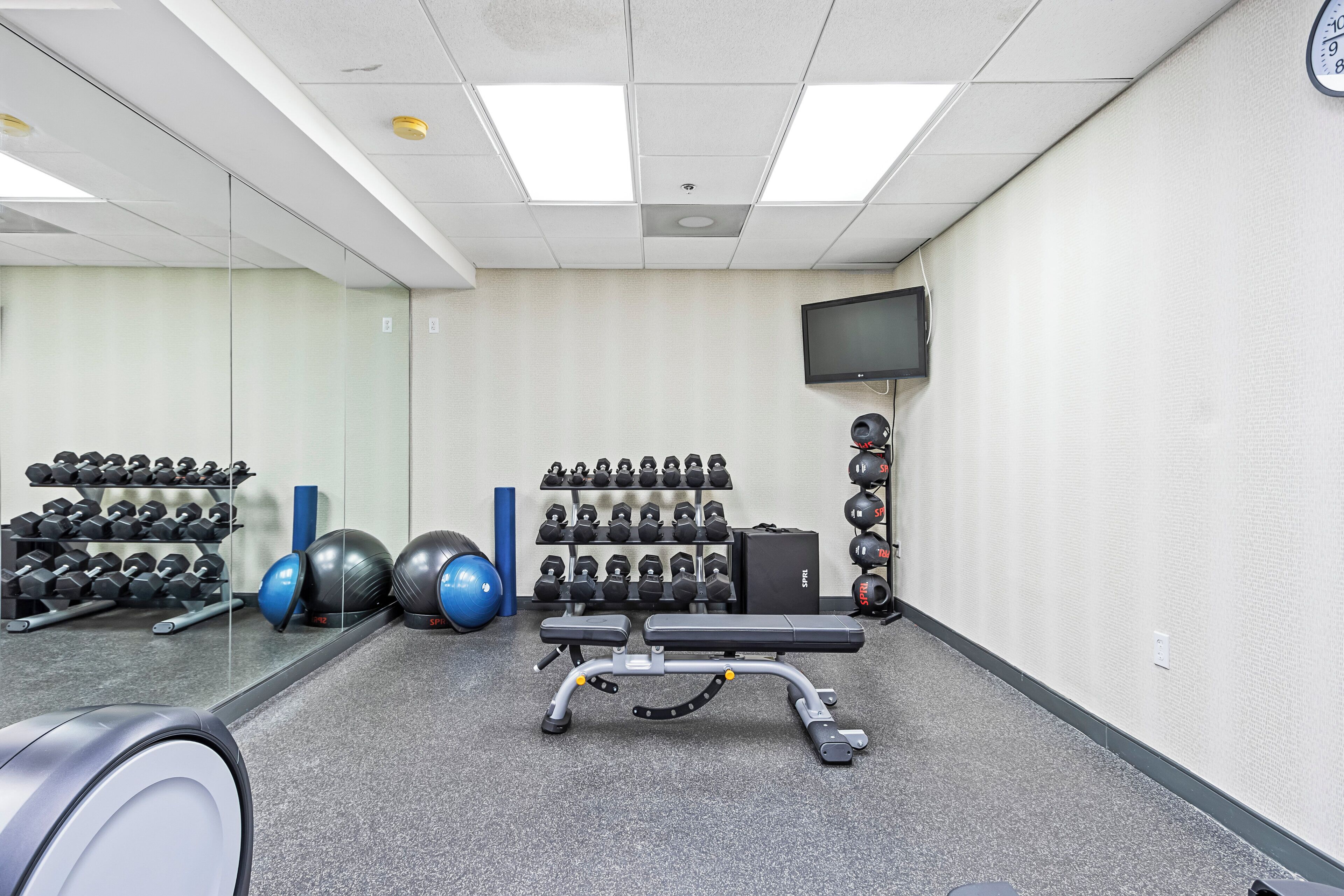 A gym with exercise equipment, a bench, and a television on the wall.